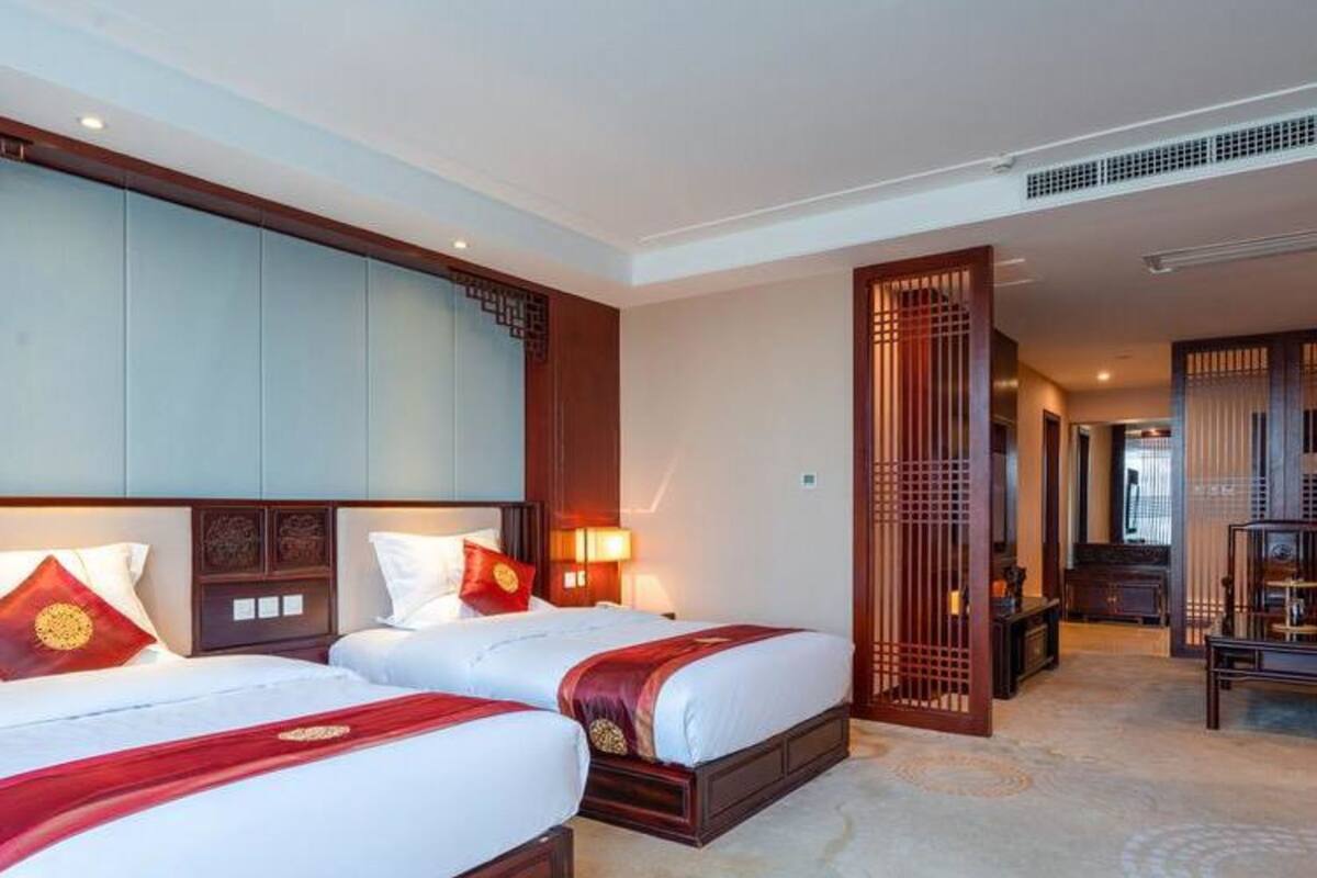 A hotel room with two beds, a large wardrobe, a desk, and a traditional decorative screen.