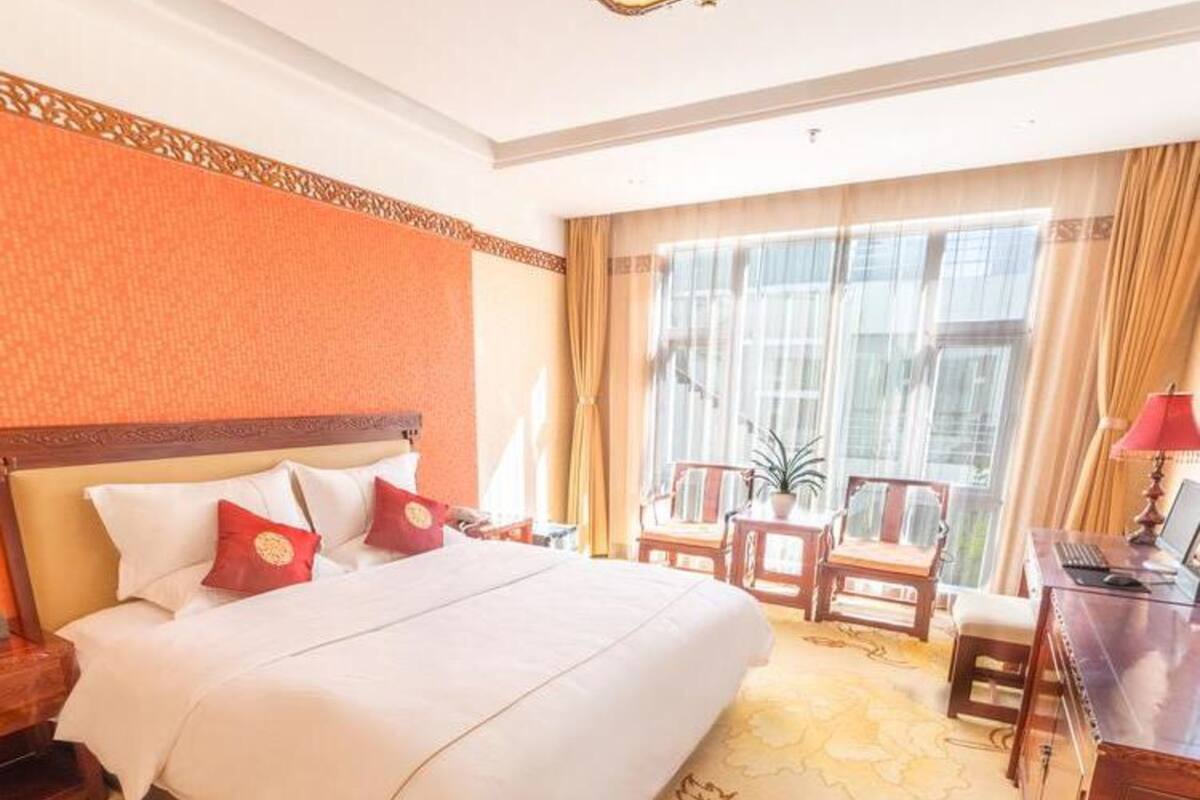 A hotel room with a large bed, a desk with a computer, and a window with curtains.