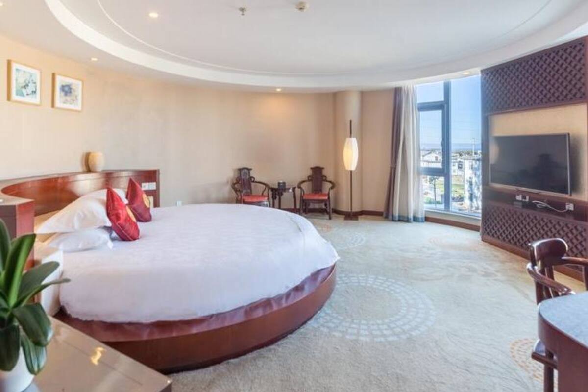 A hotel room with a large bed, a TV, a desk, and a view of the city.