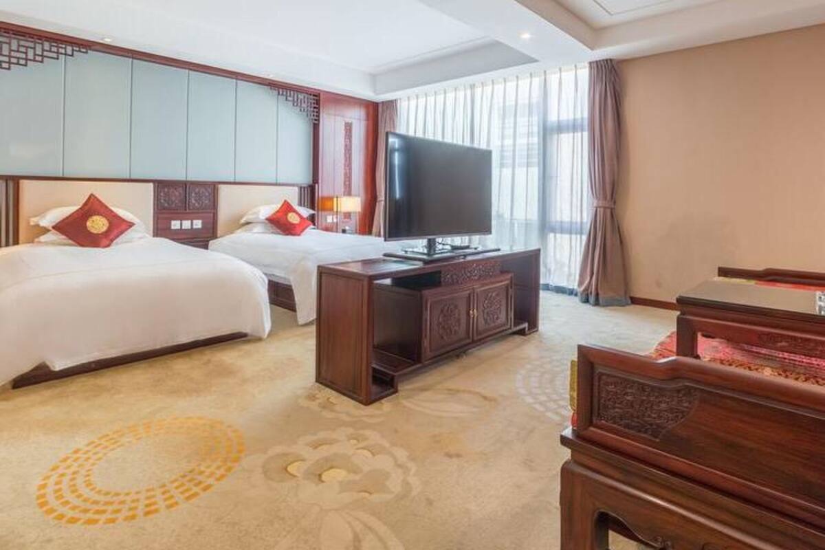 A hotel room with two beds, a television, a wooden cabinet, and a piano.
