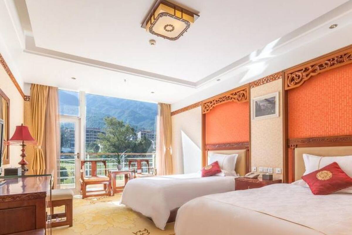 A hotel room with two beds, a desk, a chair, and a view of the outdoors.