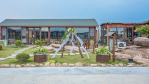 A building with large windows, a stone pathway, and a rock garden. - Floral Hotel Qingdao Shark Stone (Qingdao)