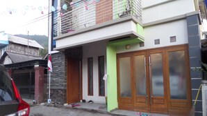 Uma casa moderna de dois andares com varanda, um carro estacionado na frente e uma rua com poças.