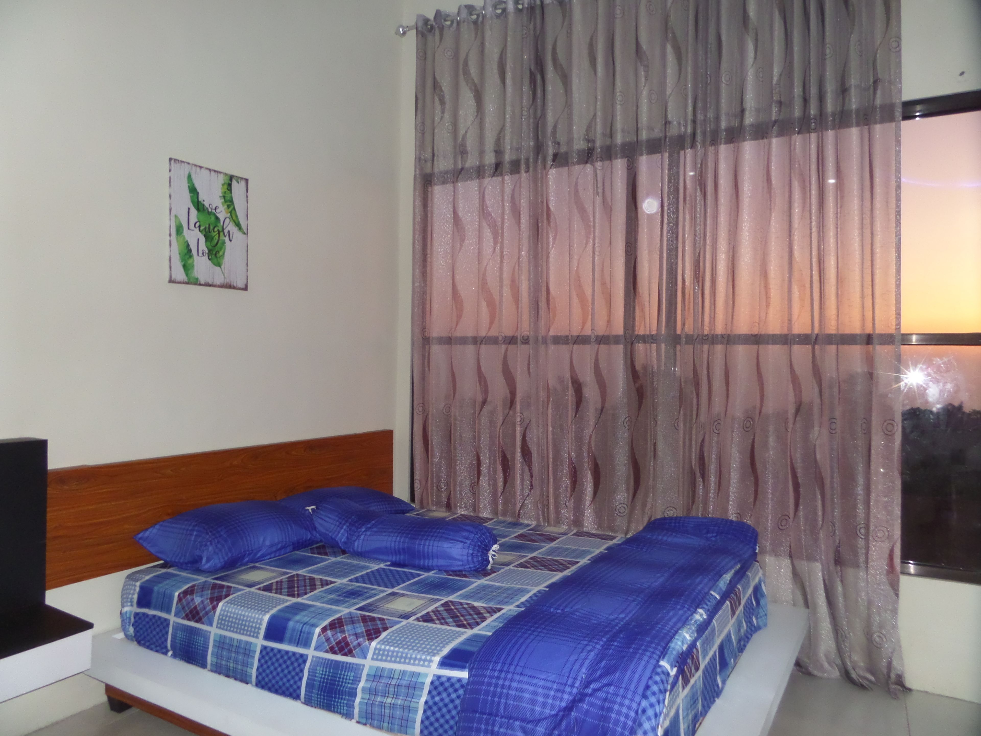 Un dormitorio con cama, cabecero, ventana con cortinas e imagen colgada en la pared.
