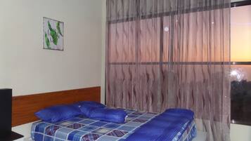 Un dormitorio con cama, cabecero, ventana con cortinas e imagen colgada en la pared.
