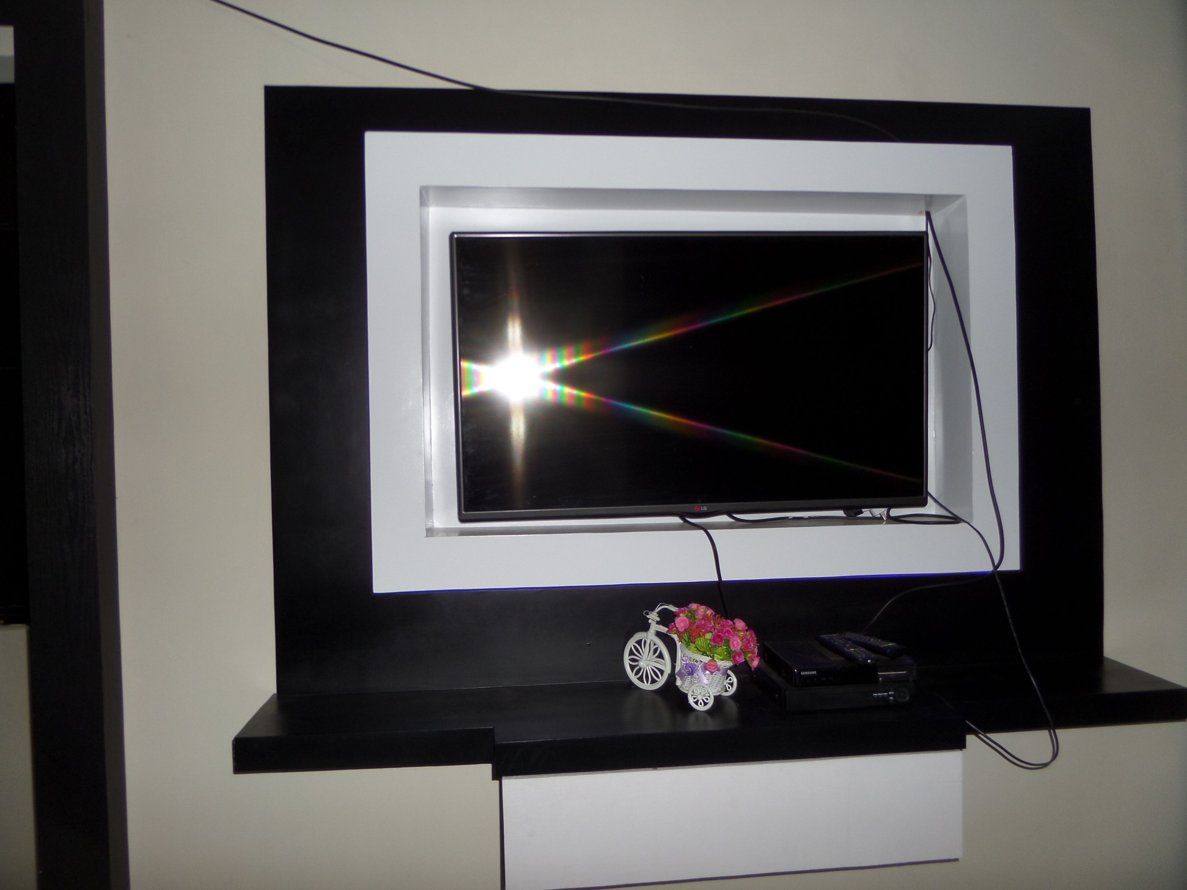 A television mounted on a black and white wall, with a small decorative item below it.