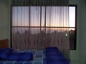 A room with a large window, two beds with blue bedding, and a curtain. - Rumah Singgah BRM (Sukapura)