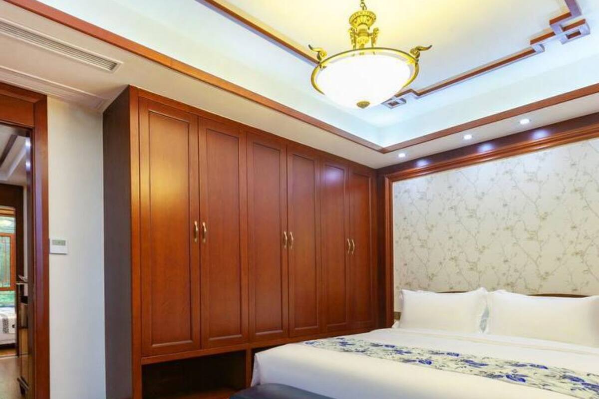 Ein Schlafzimmer mit einem großen Bett, einem Holzschrank, einer Sitzbank und einer Pendelleuchte.