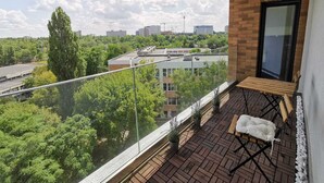 Een balkon met uitzicht op een stadsbeeld, een houten bankje en bloempotten.