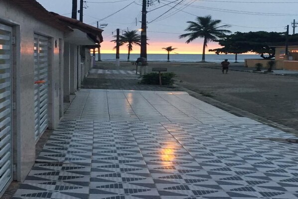 A tiled walkway leading to a beach with palm trees and a sunset in the background.