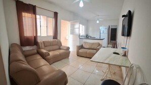 A living room with two sofas, a dining table, and a kitchen area with a refrigerator and microwave.