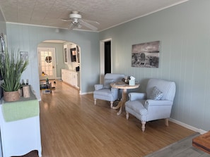 A living room with striped chairs, a round table, a ceiling fan, and a painting on the wall. - Caribbean-Blue Elk Lake Escape Remodeled 6BR Waterfront Retreat. (Kewadin)