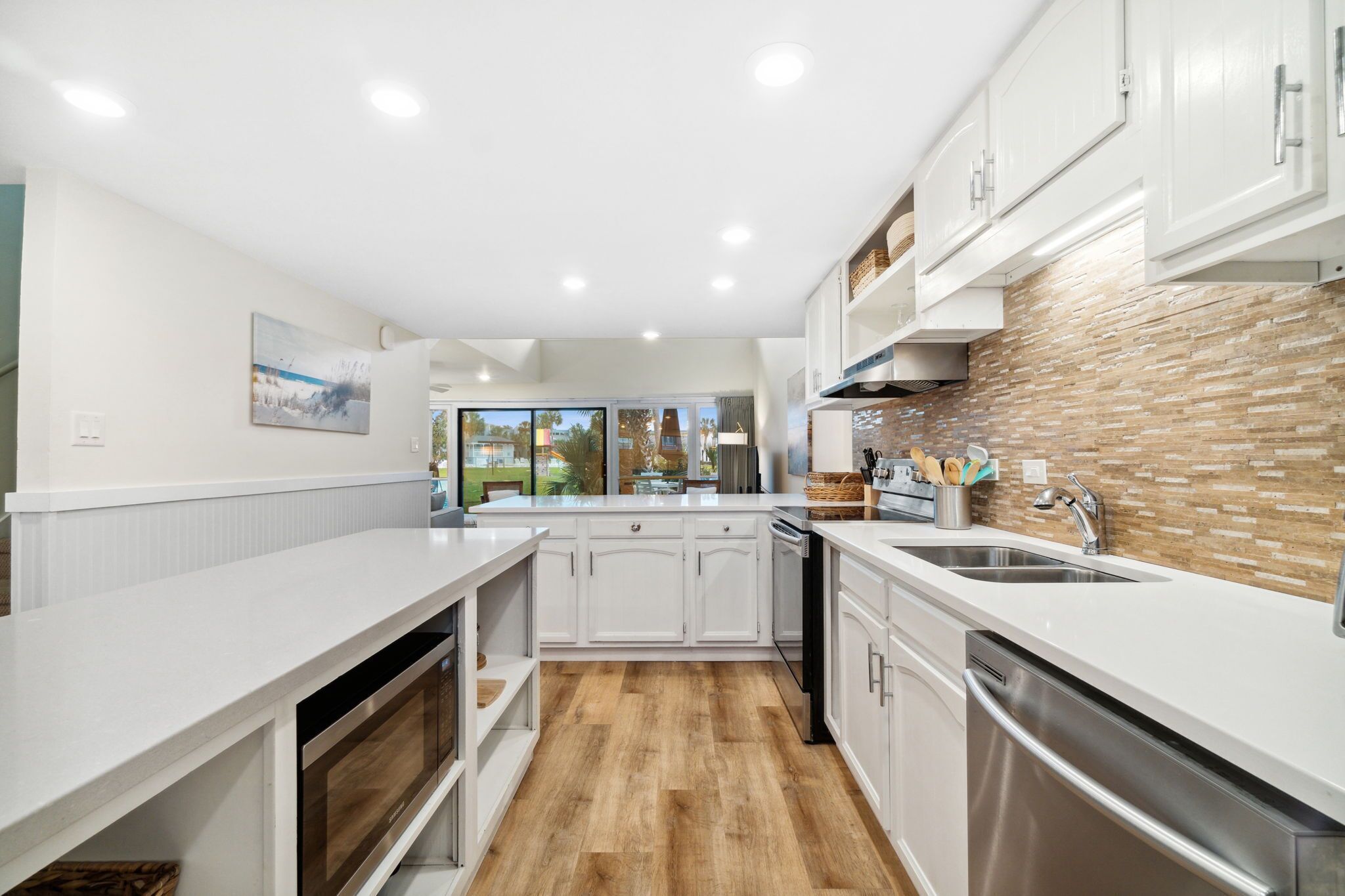 Uma cozinha moderna com armários brancos, painel de backsplash de tijolos e piso de madeira.