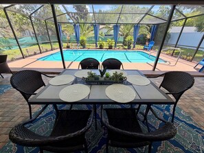 An outdoor patio with a table set for four, surrounded by wicker chairs, overlooking a swimming pool. - Cozy cottage.New Port Richey.Private Heated Pool-solar panels. (NEW PORT RICHEY)