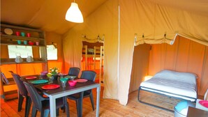 Een tentaccomodatie met een eethoek, een bed en een raam met gordijnen.