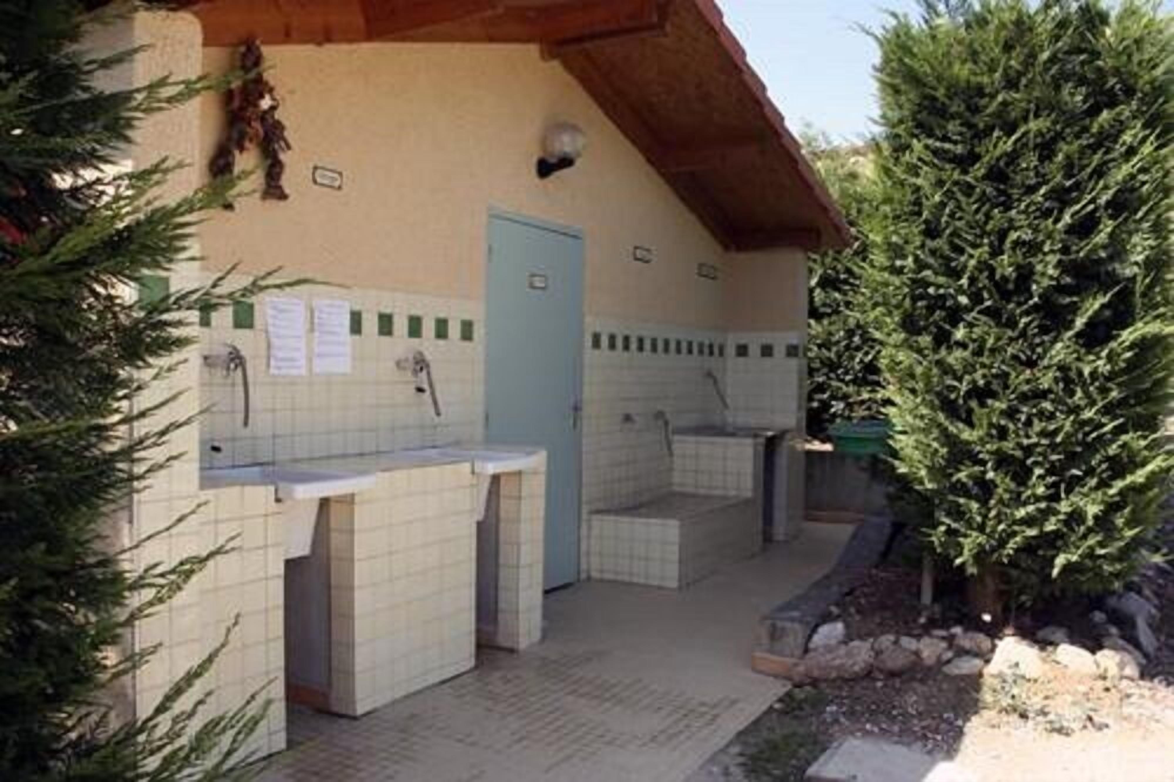 Un bâtiment à l’extérieur recouvert de tuiles, avec une porte et un petit arbre au premier plan.