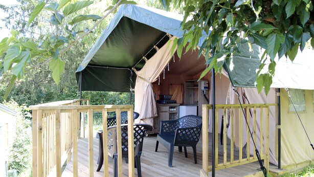 Een houten terras met een overdekte zithoek, een keuken en een slaapgedeelte in een tentvormige constructie.