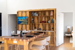 A dining area with a wooden table and chairs, a bookshelf with books, and a television mounted on the wall.