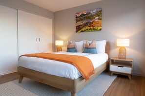 A bedroom with a bed, bedside tables, a painting on the wall, and a wardrobe. - Dock of the Bay (Coles Bay)