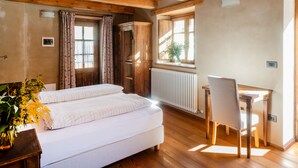 Un dormitorio con techo de madera, una cama con ropa de cama blanca, un escritorio de madera y un radiador.