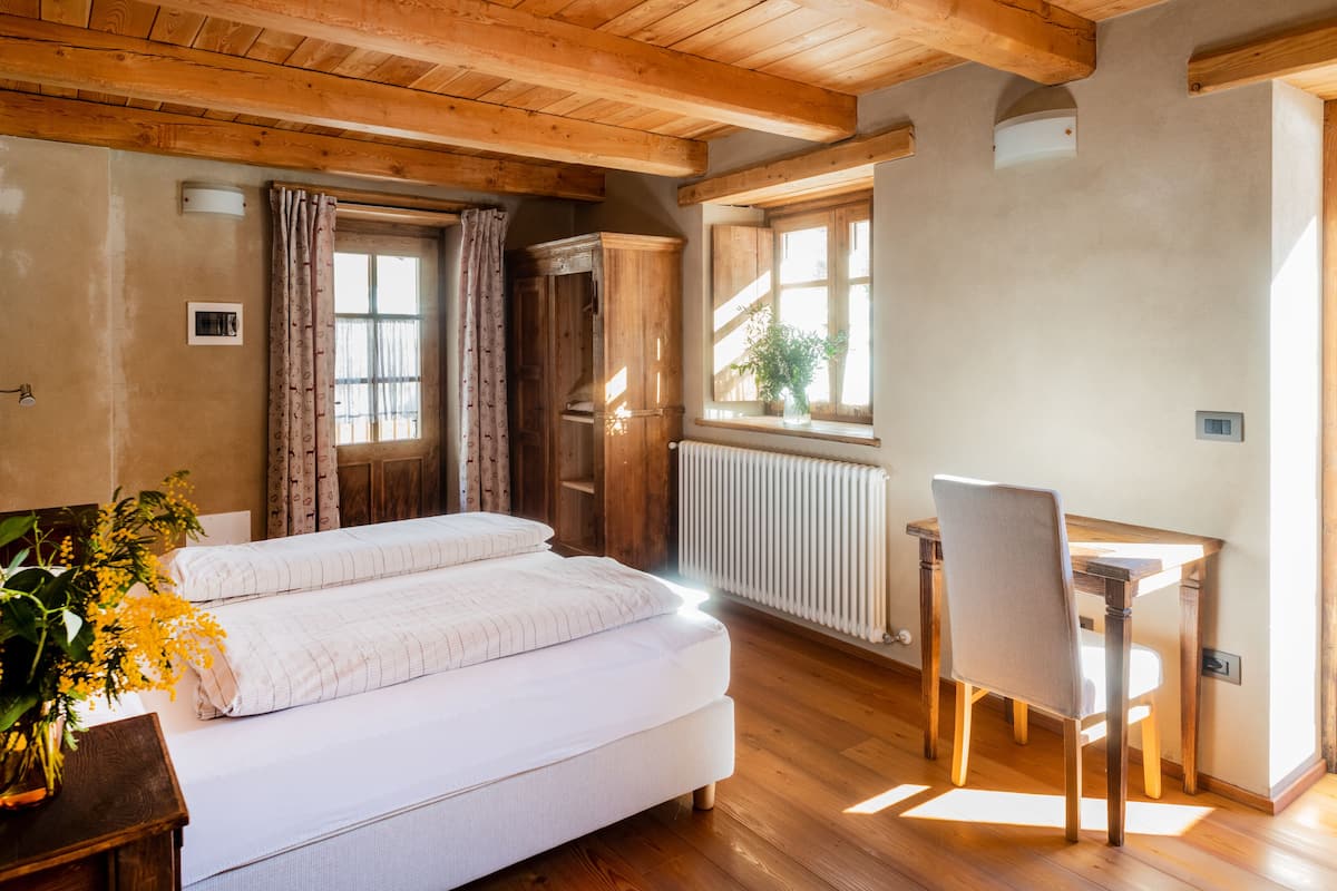 A bedroom with a wooden ceiling, a bed with white bedding, a wooden desk, and a radiator.