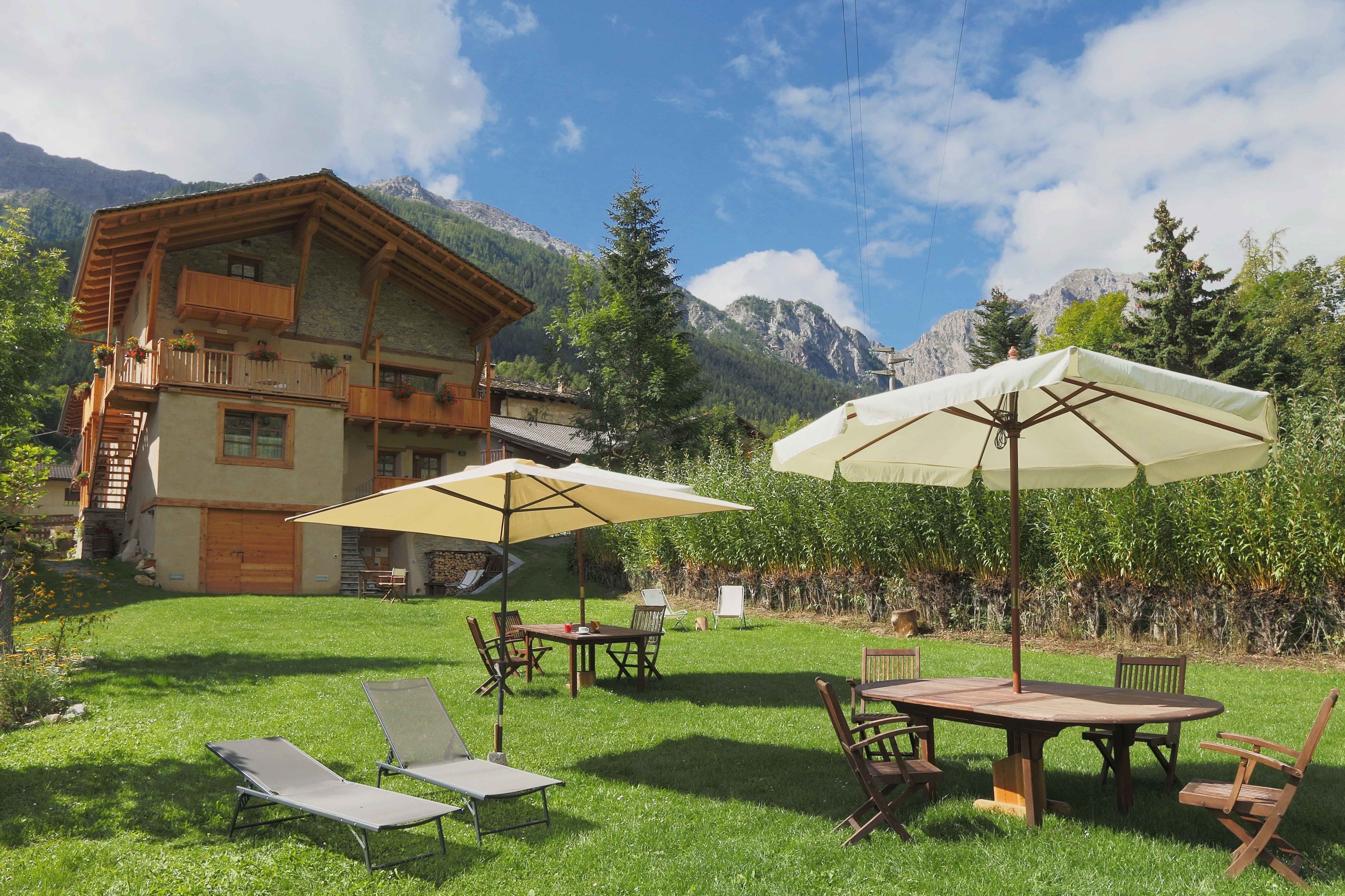 Un chalet doté d’un balcon en bois, d’un coin repas avec des tables et des chaises, et d’un grand parasol.