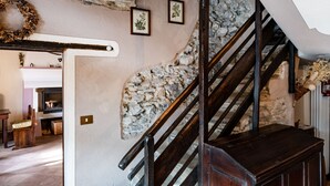Un muro de piedra con una escalera de madera y una chimenea al fondo.