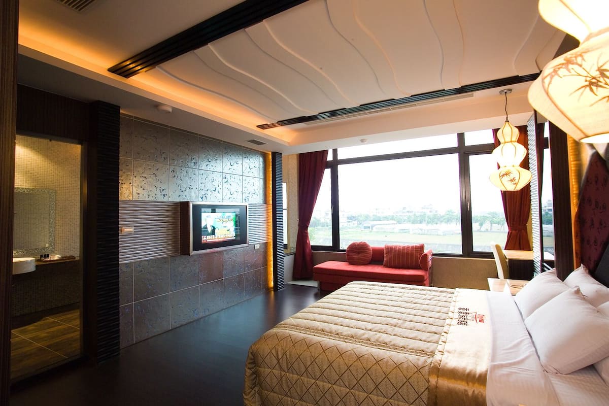 Una habitación de hotel moderna con una cama grande, un televisor montado en la pared y vistas al exterior a trav és de la ventana.