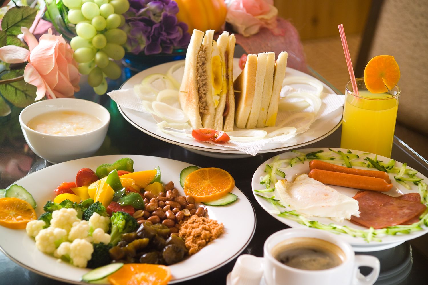 Une table avec divers aliments pour le petit-déjeuner, notamment des sandwichs, des fruits, des légumes et un verre de jus d’orange.