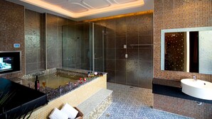 Un baño moderno con ducha de vidrio, una bañera grande con detalles de mosaico y un tocador con espejo.
