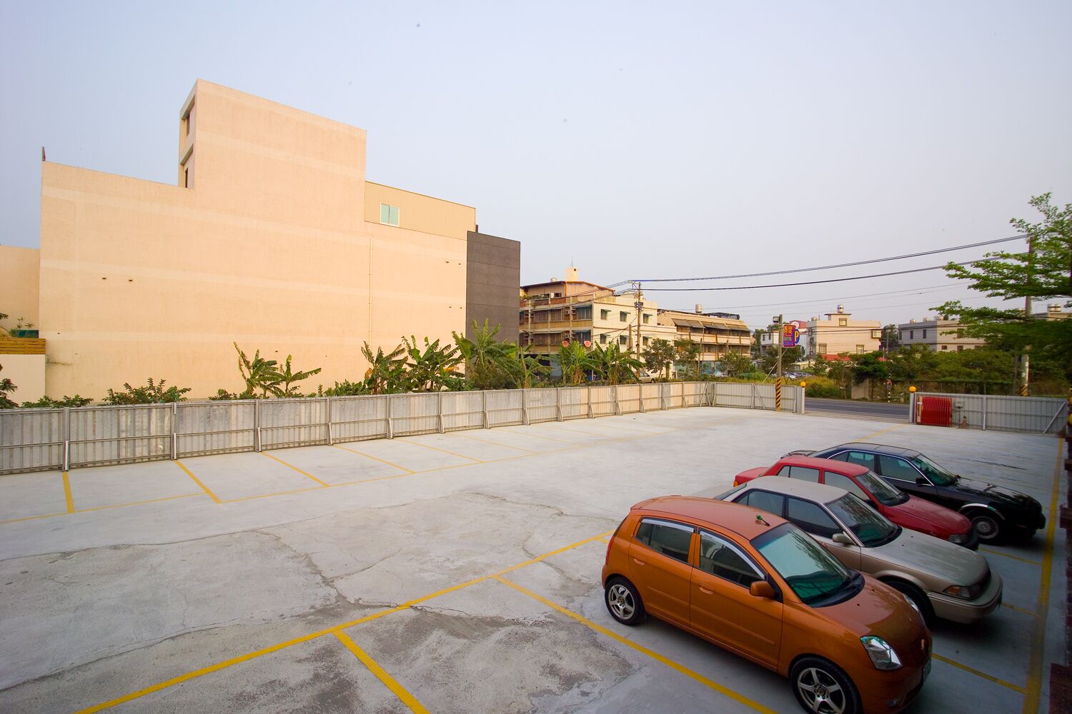 A parking lot with several cars, a concrete wall, and buildings in the background.
