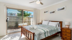 Une chambre à coucher comprenant un lit, des tables de chevet et donnant sur un espace extérieur grâce à une porte coulissante.