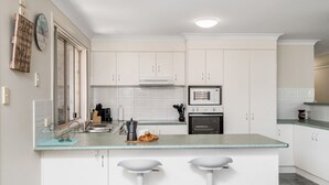 Een moderne keuken met witte kasten, een inbouwoven, een magnetron en een groot schiereiland met twee barkrukken.