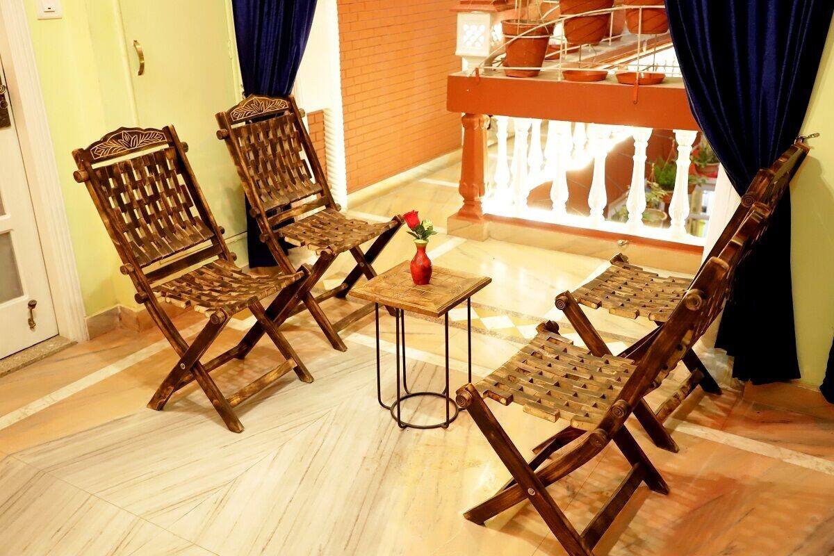 A room with two wooden chairs and a small table, a potted plant, and a window with curtains.