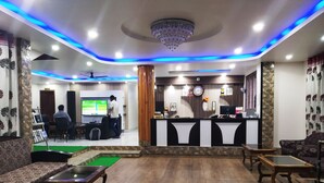 A hotel lobby with a reception desk, seating area, and a television screen.