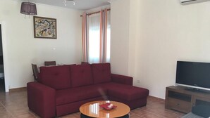 Un salon avec un canapé rouge, une table basse ronde et un téléviseur posé sur un meuble en bois.