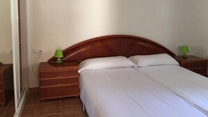 Une chambre à coucher avec une tête de lit en bois, un lit simple avec une literie blanche, deux tables de chevet avec des lampes vertes et une table de nuit en bois.