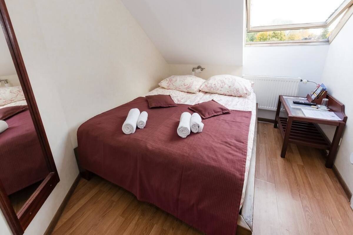 A bedroom with a bed, pillows, a wooden nightstand, and a window.