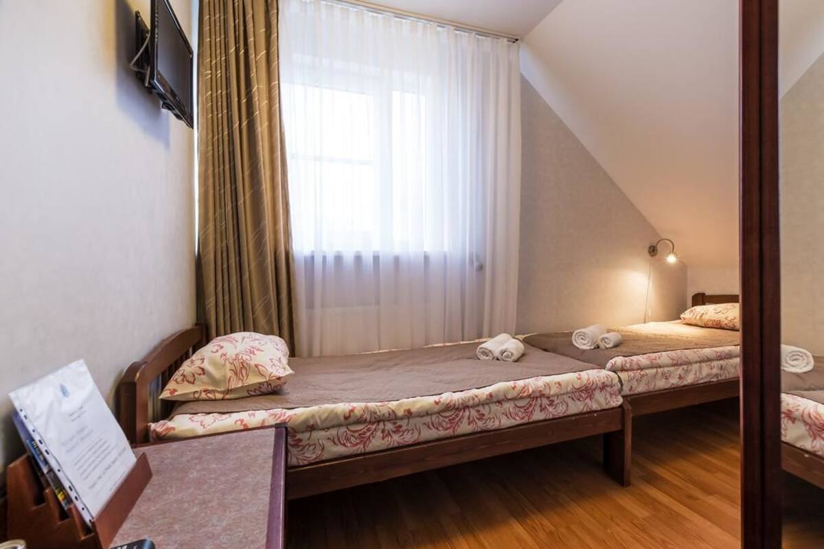 A bedroom with two beds, a desk with a laptop, and a TV mounted on the wall.