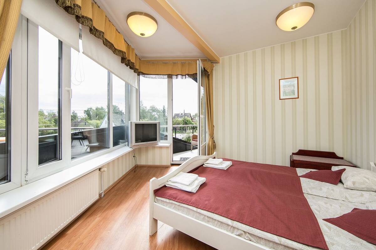 A bedroom with a large window, a bed, a TV, and a view of the outdoors.