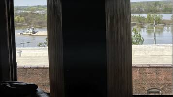 Ein Zimmer mit großem Fenster mit Blick auf einen Fluss, einer Ziegelwand und einem Holzboden.