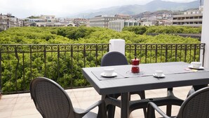 A balcony with a table set for two, overlooking a cityscape with buildings and greenery. - Le Stanze di Piazza Cairoli (Messina)