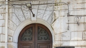 A large wooden double door with a decorative glass panel above it, set in a stone building with a plaque on the wall to the right. - Le Stanze di Piazza Cairoli (Messina)