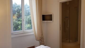 Une chambre à coucher comprenant un lit, un téléviseur, une fenêtre avec des rideaux et un espace douche.