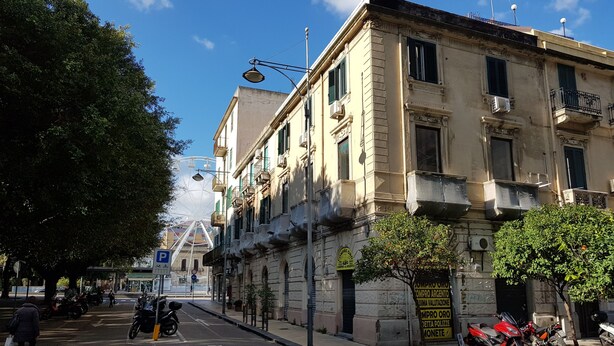 A street view with a building featuring a sign for a goldsmith service, parked motorcycles, and a clear blue sky. - Le Stanze di Piazza Cairoli (Messina)