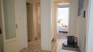 A hotel hallway with a patterned floor, a coffee machine on a counter, and a bed with a pillow in the background. - Le Stanze di Piazza Cairoli (Messina)