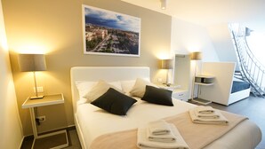 A hotel room with a neatly made bed, two bedside lamps, a cityscape painting, and a view of the outside balcony. - Le Stanze di Piazza Cairoli (Messina)