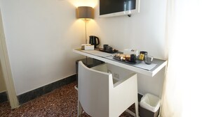 A compact hotel room with a kitchenette, a flat-screen TV, a lamp, and a small trash bin. - Le Stanze di Piazza Cairoli (Messina)