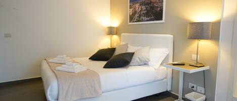 Quarto de hotel moderno com cama bem arrumada, mesa de cabeceira com abajur e pintura de paisagem urbana na parede.