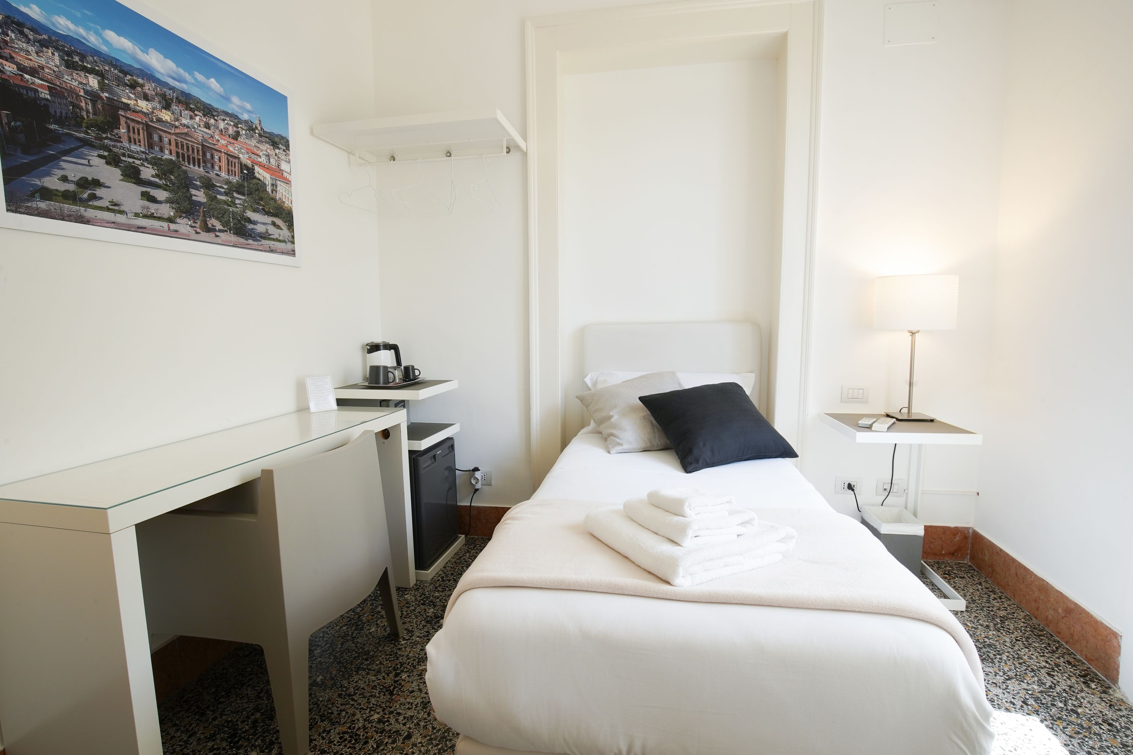 A hotel room with a bed, a desk, a chair, a lamp, and a painting on the wall.